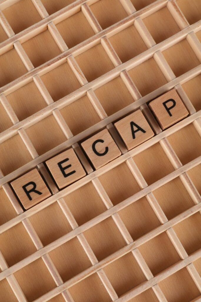 High-angle view of Scrabble tiles forming the word 'Recap' on a wooden grid.