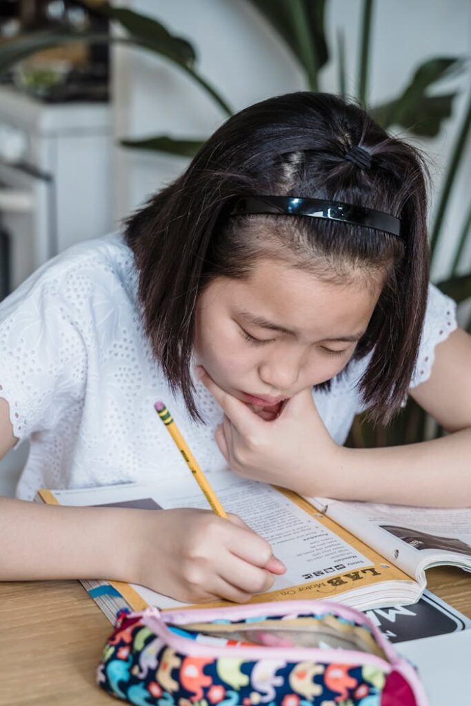Young girl deeply focused on her studies, working with a book and pencil indoors.